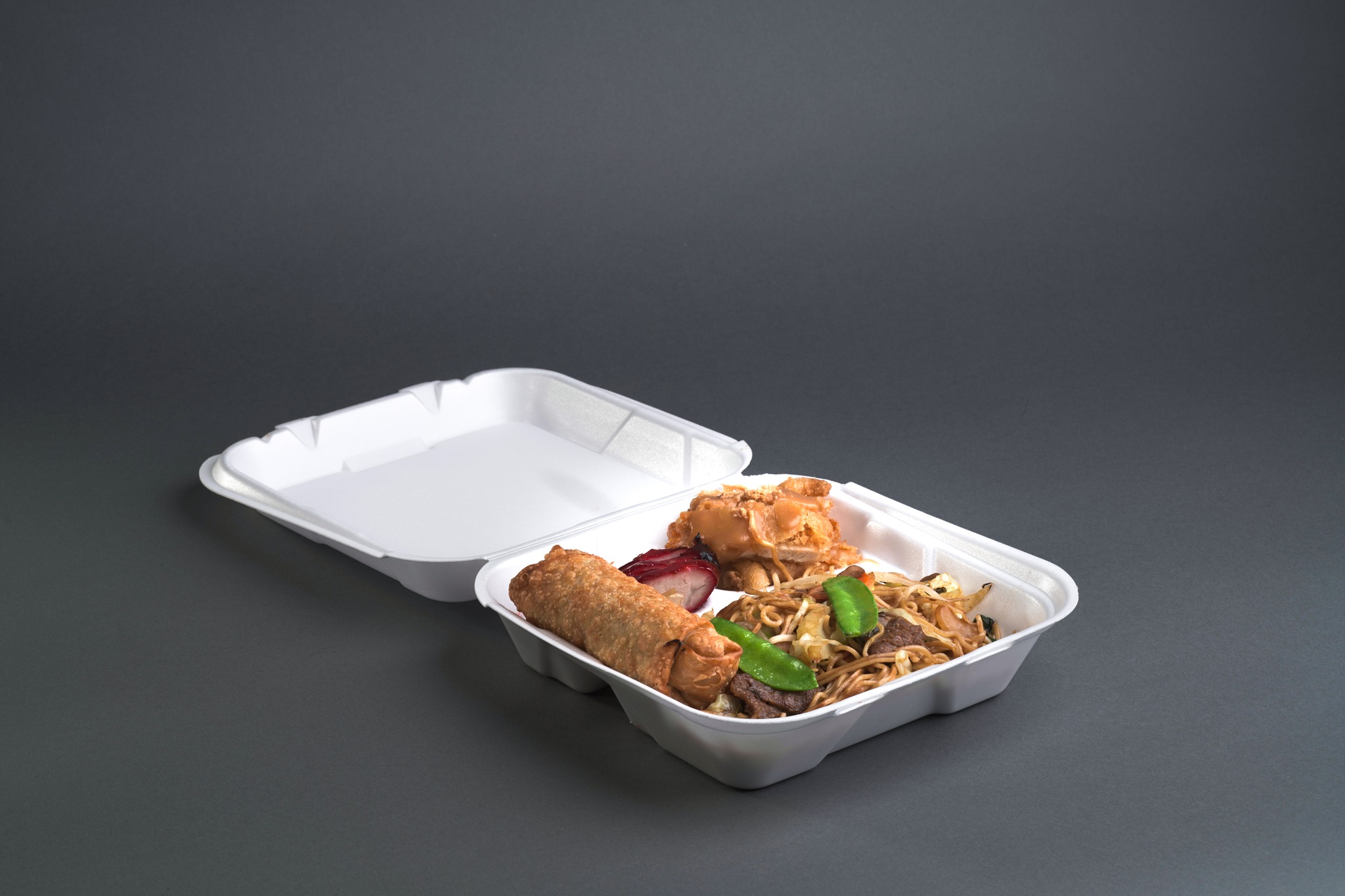 A clean open to-go box filled with noodles, an egg roll, barbecue pork and crispy chicken